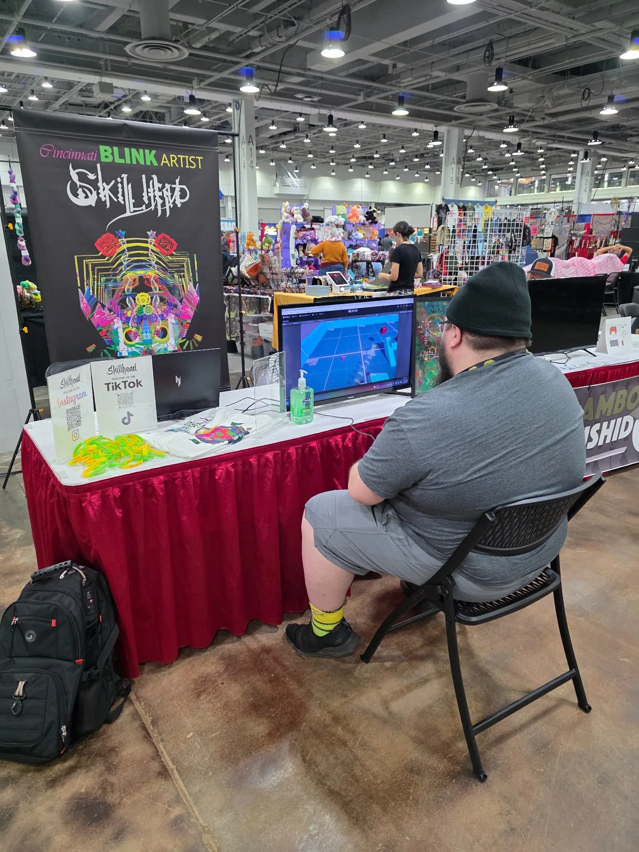 A visitor using a game controller beside Skillhead artwork at the ARBITRARY ZEN booth at Cincinnati Comic Expo 2026